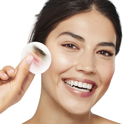 Lächelnde Frau hält ein Reinigungspad voller Make up neben ihr Gesicht