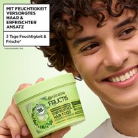 Mann mit lockigem Haar hält Fructis Multi-Use Haarmaske Kiwi Menthol Hair Food neben sein Gesicht und lächelt