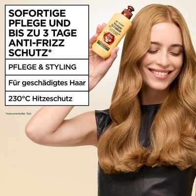 Frau hält das Wahre Schätze 2-in-1 Pflege & Styling Leave-In Creme Honig Schätze neben ihren Kopf und lächelt