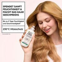 Frau hält Wahre Schätze 2-in-1 Pflege & Styling Leave-In Creme Sanfte Hafermilch Produkt neben ihr Gesicht und lächelt