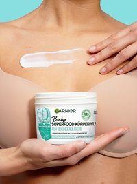 Eine Frau trägt Body Superfood Körperpflege 48h beruhigende Creme auf ihren Oberkörper auf