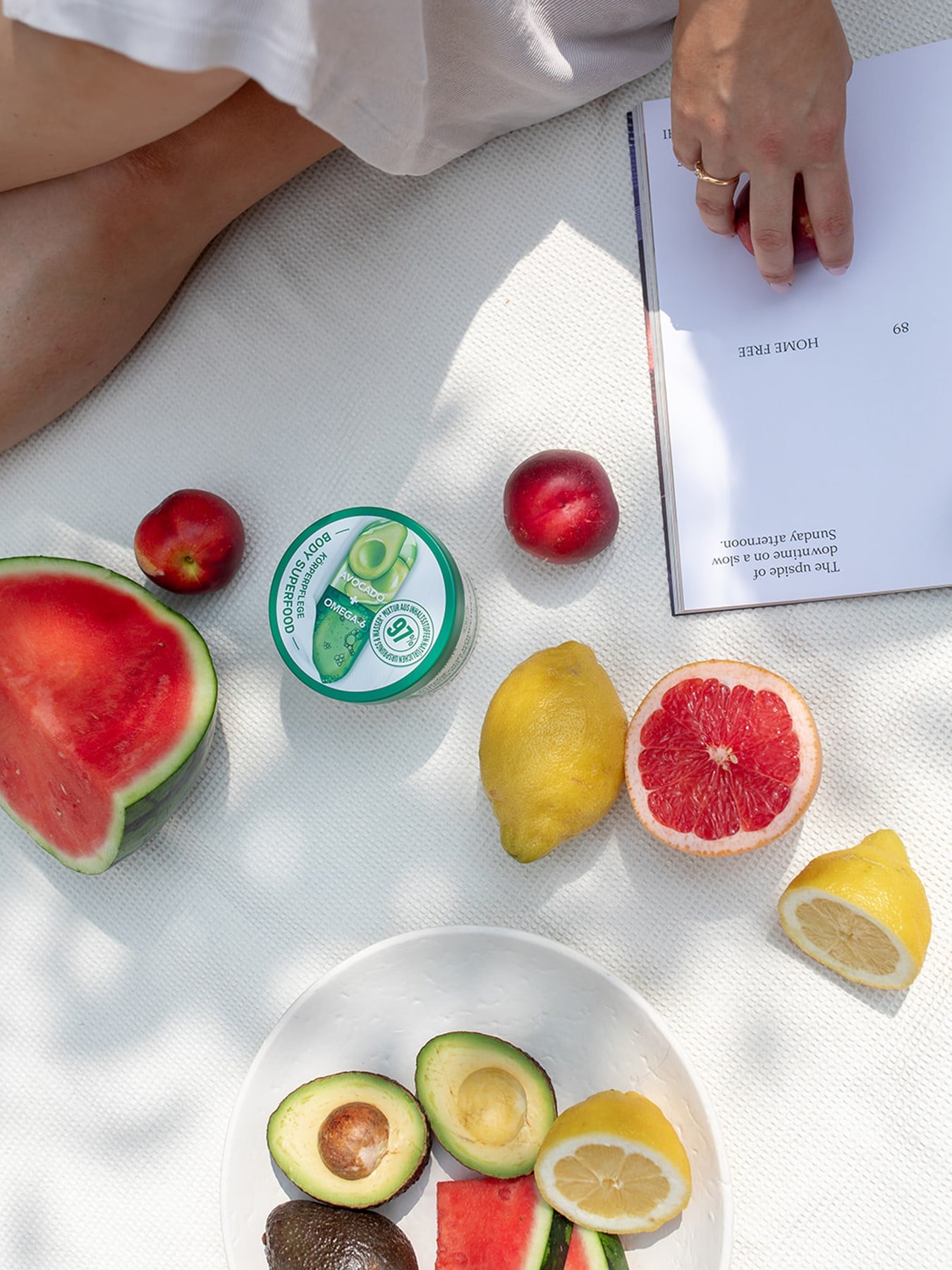 Eine Person sitzt auf einer Decke und liest ein Buch daneben liegt aufgeschnittenes Obst auf der Picknickdecke