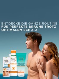 Eine junge Frau lehnt sich an einen jungen Mann sowei drei Ambre Solaire Produkten im Vordergrund