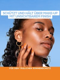 Eine junge Frau mit lockigen Haaren fühlt mit de rHand ihre Wange vor himmelblauem Hintergrund