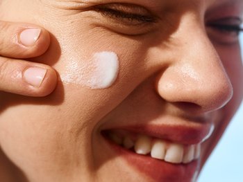Nahaufnahme einer lächelnden Person die ihr Gesicht mit einer Creme versorgt