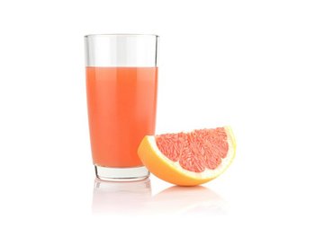 Ein Glas Grapefruitsaft, daneben ein Stück Grapefruit