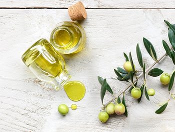 Zwei Flachen gefüllt mit Oliven-Öl daneben liegt ein Olivenzweig