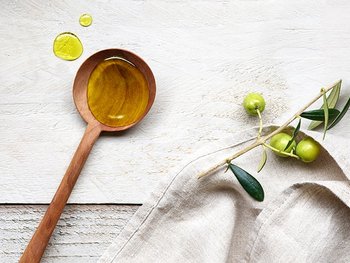 Eine Kelle gefüllt mit Oliven-Öl und ein Olivenzweig