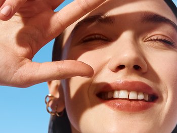 Nahaufnahme einer Frau, die ihre Hand schützend vor ihr Gesicht hält, um sich vor der Sonne zu schützen.