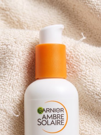 Eine Frau hält eine Flasche Garnier Sonnenschutz vor ihrem Körper