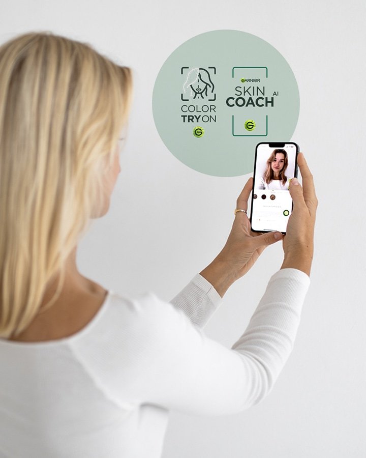 Blonde Frau hält ein Smartphone vor ihr Gesicht und testet das Virtual Try On