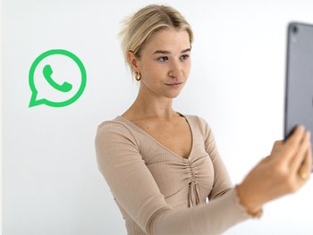 Blonde Frau hält ein Tablet vor ihr Gesicht und daneben ein WhatsApp Logo