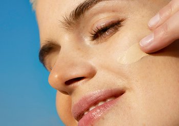 Frau trägt BB Cream mit den Fingern auf die Wange auf