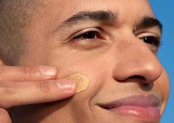 Frau trägt BB Cream mit den Fingern auf die Wange auf