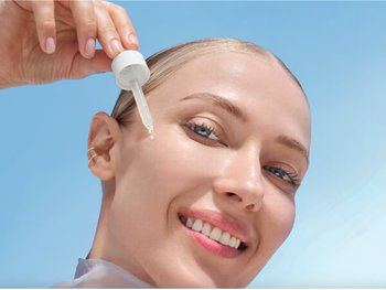 Lächelnde Frau trägt Serum aus einer Pipette auf ihre Wange auf