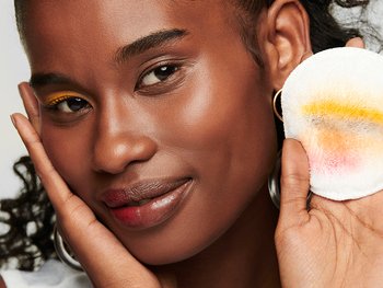 Frau hat sich das halbe Gesicht abgeschminkt und hält Reinigungspad in der Hand