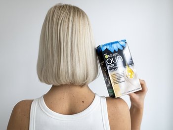 Frau mit platinblondem Haar hält den Olia Toner auf der Schulter