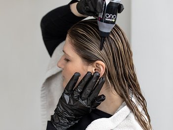 Frau mit Handschuhen trägt Coloration auf ihre Haare auf